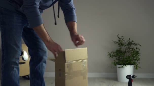 El hombre desempaca la caja de cartón, saca piezas de muebles de madera. Autoensamblaje de piezas de mobiliario — Vídeos de Stock