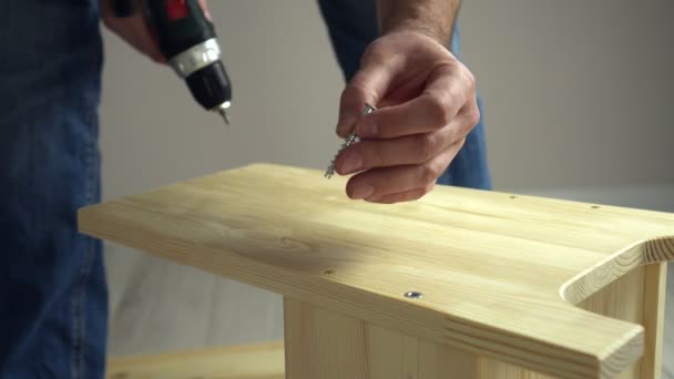 DIY furniture assembly. Craftsman drives screw into wooden board with electric powered screwdriver — Stock Video