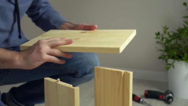 床に自宅でフラットパック家具DIYを組み立てる男。男は指示に従って家具を組み立てる — ストック動画