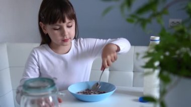 Küçük kız beyaz masada oturmuş sütlü çikolatalı mısır topu yiyor. Çocuk kahvaltı yapıyor.