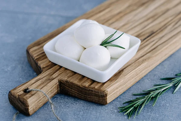 Yumuşak İtalyan beyaz peyniri mozzarella ahşap tahta üzerinde beyaz kâse içinde taze biberiye dalıyla servis edilir.