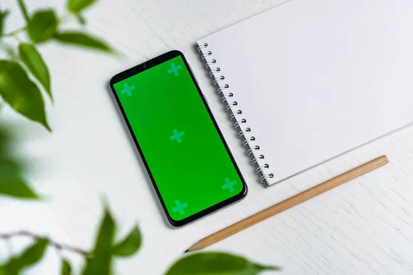 Zelená dovolená s prázdným notepadem smartphone zelený displej maketa a tužkou plochý ležel. Horní pohled — Stock fotografie