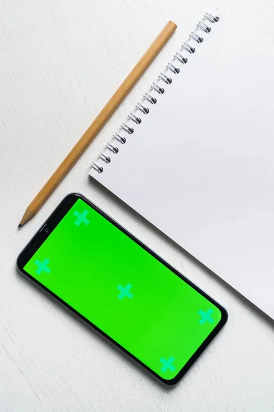 Bílý prázdný notepad smartphone zelená obrazovka maketa a tužka plochý ležel. Tamplate pro design — Stock fotografie
