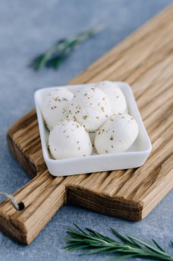 Yumuşak İtalyan beyaz peyniri mozzarella ahşap tahta üzerinde beyaz kâse içinde taze biberiye dalıyla servis edilir.