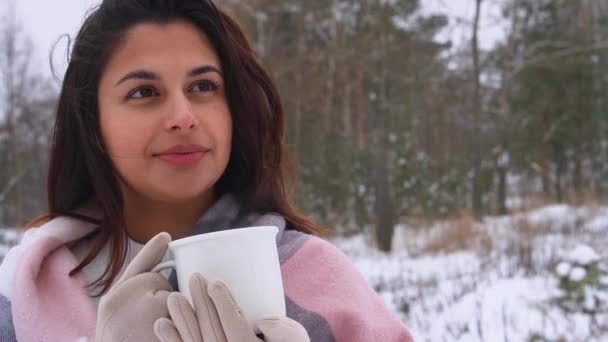 Fiatal aranyos swarthy barna nő ivás forró ital fehér kerámia csésze havas téli erdőben — Stock videók