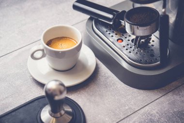 Espresso makinesi sürahisinin yanındaki masada taze kahve ve süt ile beyaz bardak.