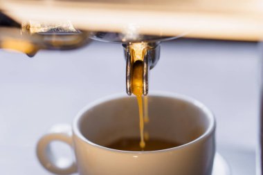 Portafilter espresso makinesinden beyaz seramik fincana taze kahve dökülüyor. Kapat.