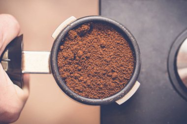 Barista elinde taze kahveyle portafilter tutuyor. Kahveyi kurcalayıcı ile hazırlıyor. Kapat.