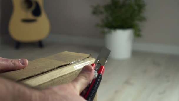 Feche as mãos dos homens caixa de papelão aberta com faca em casa inteerior. Pacote de unboxing — Vídeo de Stock