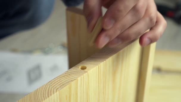 El hombre ensambla muebles atornillando tablas con pernos, manos de cerca. Montaje de estante de madera en casa — Vídeos de Stock