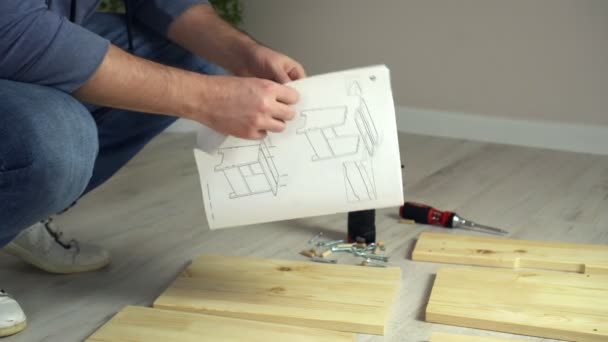 Man monteert flat pack meubels doe-het-zelver thuis op de vloer. Man monteert meubels volgens instructies — Stockvideo