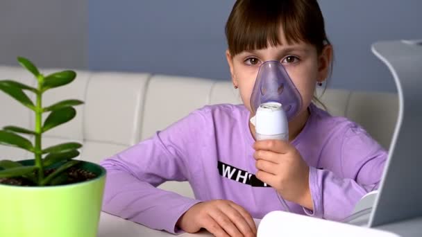 Niña hace inhalación con nebulizador médico mientras está sentada en la mesa mirando a la cámara — Vídeos de Stock
