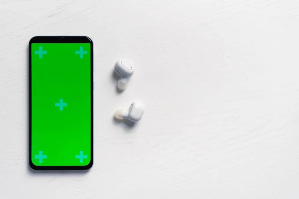 Smartphone se zelenou obrazovkou mockup a bílé bezdrátové sluchátka izolované na bílém pozadí — Stock fotografie