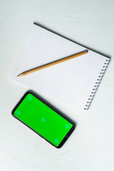 Bílý prázdný notepad smartphone zelená obrazovka maketa a tužka plochý ležel. Tamplate pro design — Stock fotografie