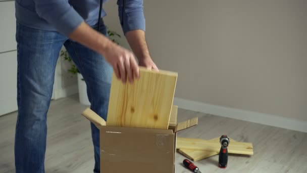 De mens pakt de kartonnen doos uit, neemt stukken houten meubilair mee. Zelfassemblage van meubelonderdelen — Stockvideo