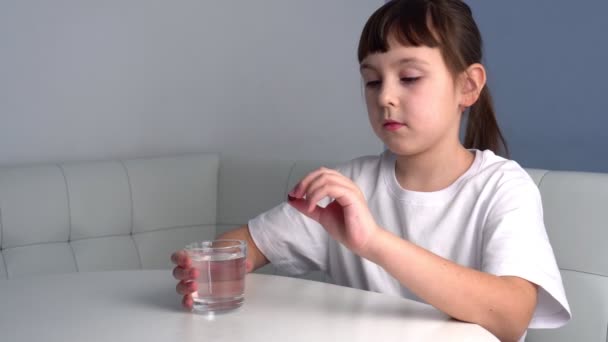 Nettes Kind im T-Shirt nimmt Medikamente und trinkt ein Glas Wasser. Kleines Mädchen nimmt Pille oder Vitamin — Stockvideo