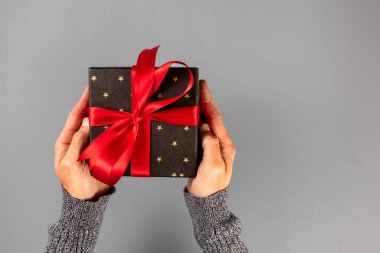 Elinde hediye tutan bir adam. Kırmızı pruva. Gri arka plan. Noel ya da Sevgililer Günü. Düz üst görünüm.