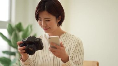 Tek lensli refleks kamera ve akıllı telefonla çekilen görüntüleri izleyen bir kadın.