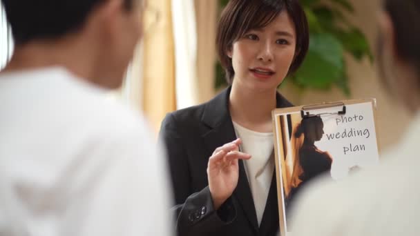 顧客に結婚式の計画を示す黒のスーツの若い日本人従業員 — ストック動画