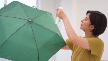 A woman spraying a water repellent spray on a folding umbrella 