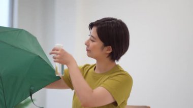 A woman spraying a water repellent spray on a folding umbrella 