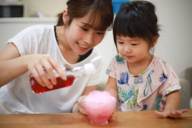Parent and child sprinkling syrup on shaved ice 
