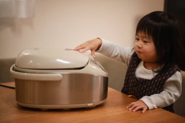 Küçük Japon kız ahşap masada multicooker açmaya çalışıyor.