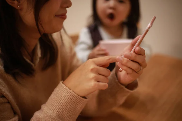 Ung Asiatisk Mamma Använder Smartphone Hemma Med Sin Dotter Bakgrunden — Stockfoto