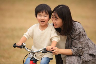 Genç Asyalı anne oğluna parkta bisiklet sürmeyi öğretiyor.
