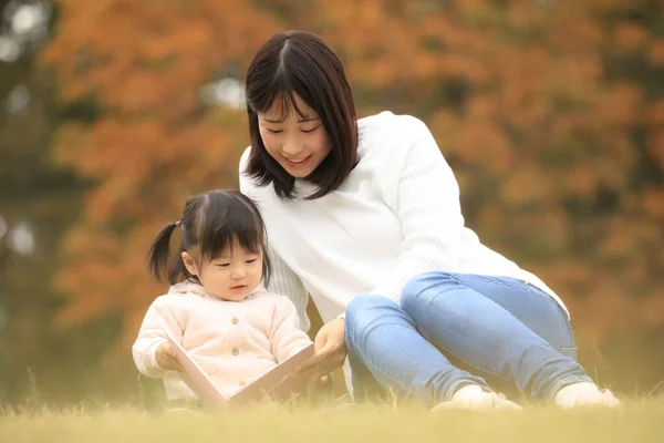 Young Japanese Woman Reading Book Her Daughter Park — Stockfoto