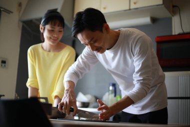 Genç bir çift evdeki mutfakta yemek pişiriyor.