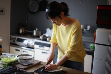 Genç Asyalı kadın mutfakta yemek pişiriyor. 