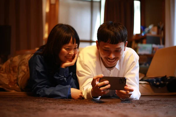 Счастливая Молодая Азиатская Пара Лежит Полу Помощью Мобильного Телефона — стоковое фото