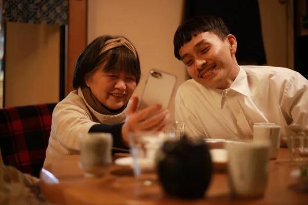 Gülümseyen Kıdemli Asyalı Kadın Genç Adam Mutfakta Oturmuş Akıllı Telefonla — Stok fotoğraf