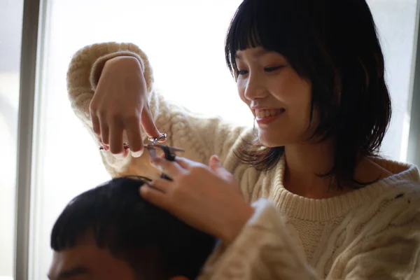 アジア系の若い女性がはさみで髪を切って笑顔の男に — ストック写真