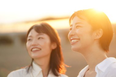 İki genç Asyalı kadın gün batımında poz veriyor.