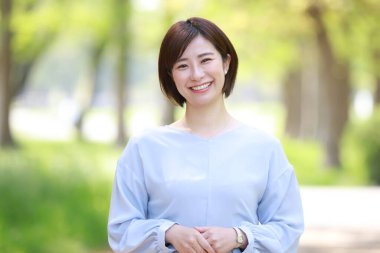 Güzel genç Asyalı kadın parkta duruyor ve kameraya gülümsüyor.