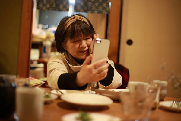 アジア系のシニア女性がテーブルに座りスマートフォンを使って — ストック写真