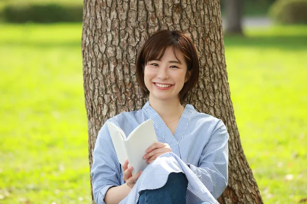 一个微笑的女人在公园看书 — 图库照片