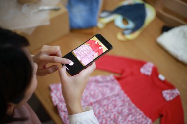 Genç bir kadın masada oturuyor ve internette satmak için giysi fotoğrafları çekiyor.