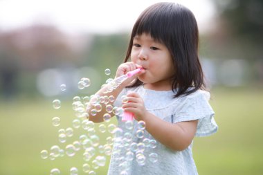 Küçük Japon kız parkta sabun köpüğü üflüyor.