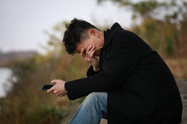 Genç Asyalı adam arka planda akıllı telefon kullanıyor.