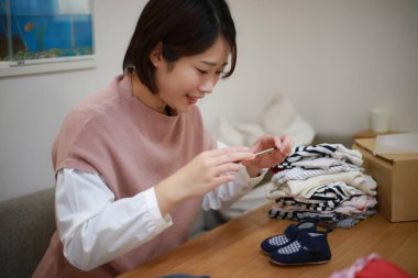 Genç bir kadın masada oturuyor ve internette satmak için giysi fotoğrafları çekiyor.