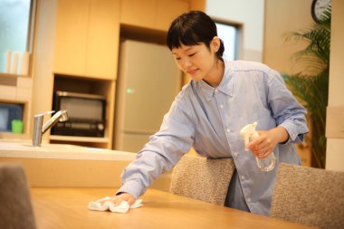 Asyalı kadın mutfak masasını bez parçasıyla temizliyor.