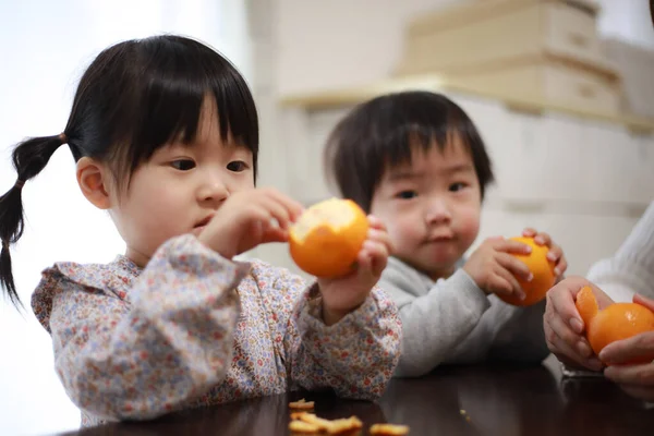 オレンジの皮をむいたアジア系の子供たち — ストック写真