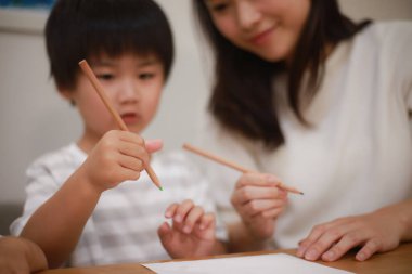 Anne çocuğuna kalem tutmayı öğretiyor.