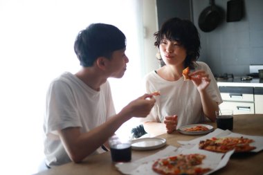 Genç bir çift mutfakta pizza yiyor.