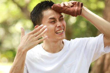 Stresli Asyalı adam terini havluyla temizliyor.