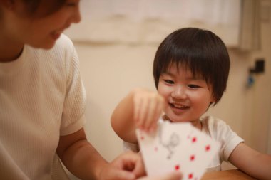 Asyalı anne ve oğlu birlikte kağıt oynuyorlar. 