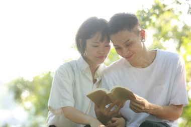 Asyalı çift yeşil çayır üzerine kitap okuyor